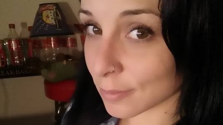 A close up photo of Ashley Simpson, who is looking towards the camera with a slight smile her face. She has shoulder length, brown hair and brown eyes and nose piercing. 