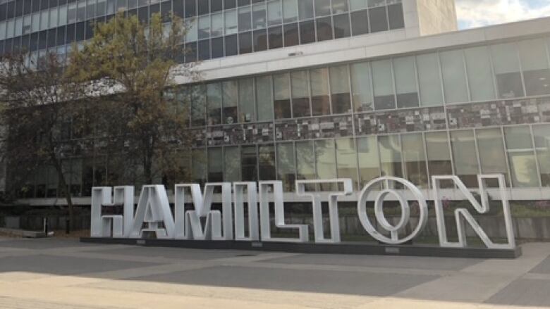 A large glass building with a sign reading HAMILTON in front is seen on a sunny day