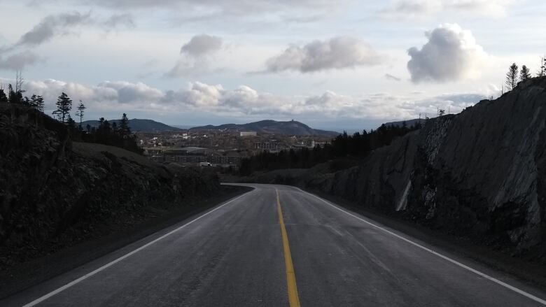 A road with a single yellow line in the middle. Rock walls rise on either side.