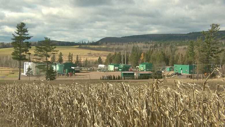 Industrial facilities and equipment can be seen in the background of a farmer's field.