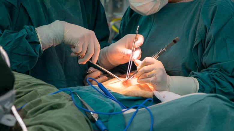 The hands of two doctors wearing green scrubs are shown holding surgical tools against a patient's skin.