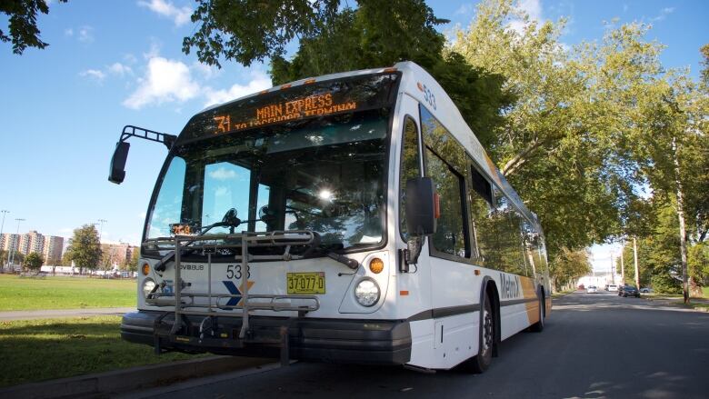 The front of a Halifax Transit bus is seen from a low angle on a roadway, with trees in the background