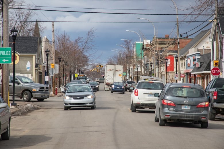 Cars drive down a street with shops and homes on either side