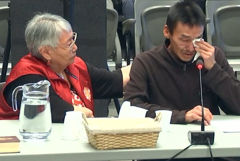 A man cries sitting at a table next to a woman 