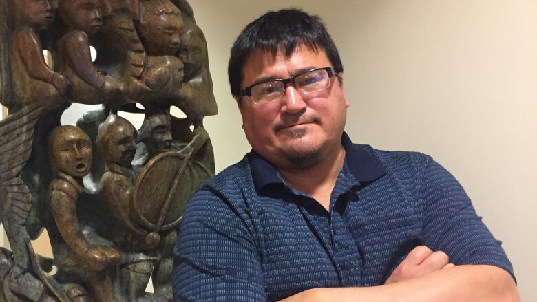 A man in glasses poses in front of a large sculpture inside a building.