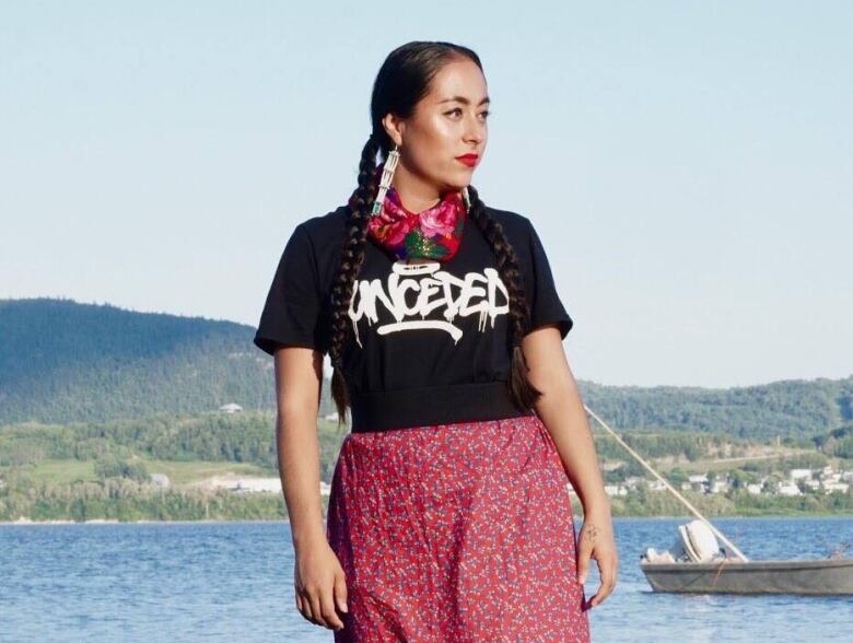 A woman in a black t-shirt and red skirt stands on the shore.