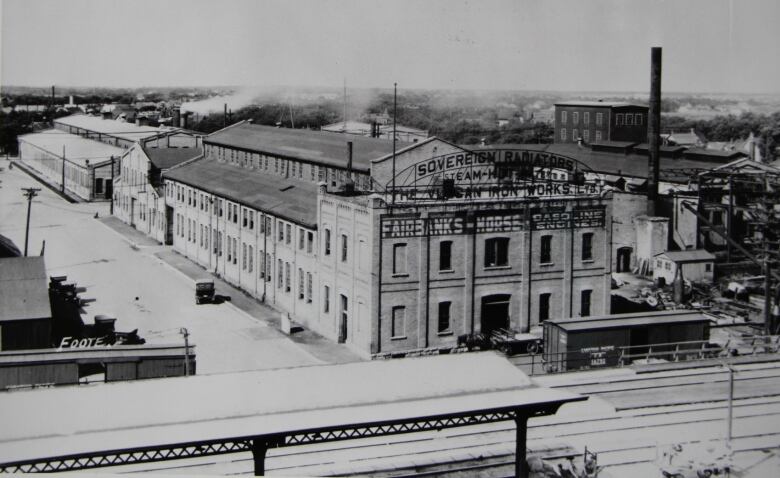 A black-and-white photo shows a complex of buildings next to a railway line.