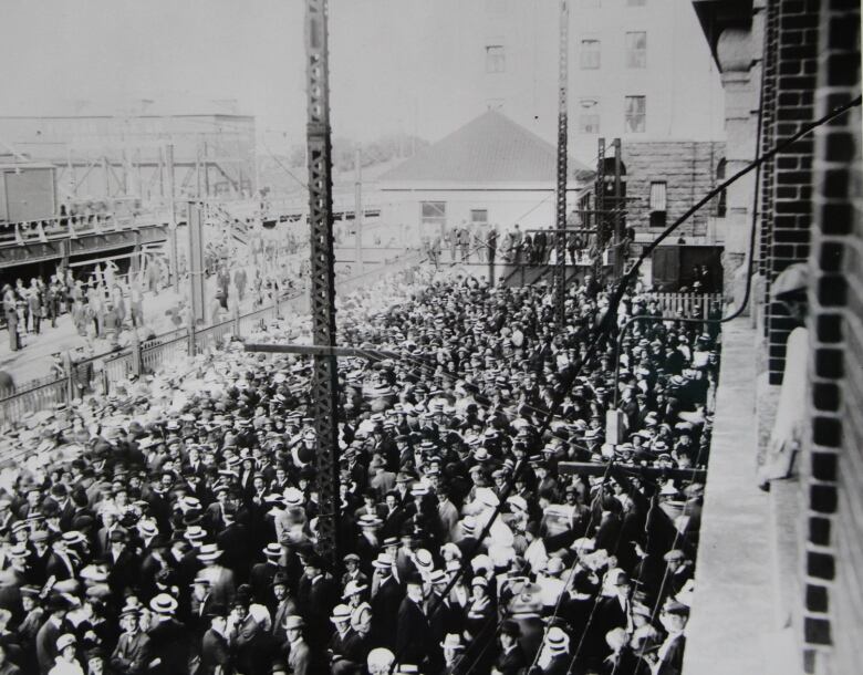 An archival photo of a large crown of men standing outside an industrial building.