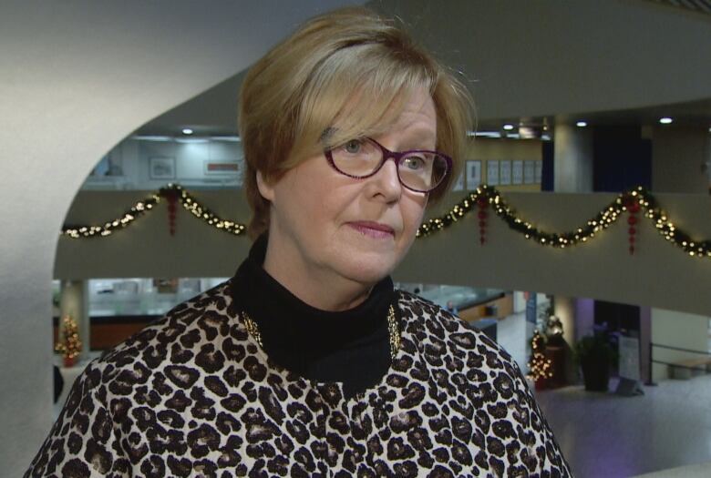 A woman and cheetah print, a black turtleneck and glasses looks off to the side of the camera. 