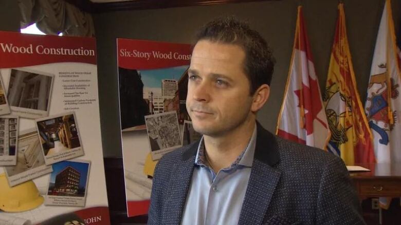 A man standing in front of two posters about wood construction and three flags.