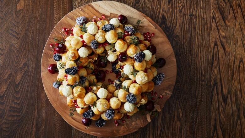 Overhead shot of a bunch of Profiteroles arranged into the shape of a wreath on a wooden cutting board. 