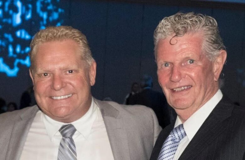 Two middle-aged white men smile with an arm around each other's shoulder, posing for the camera. One is the premier of Ontario. 