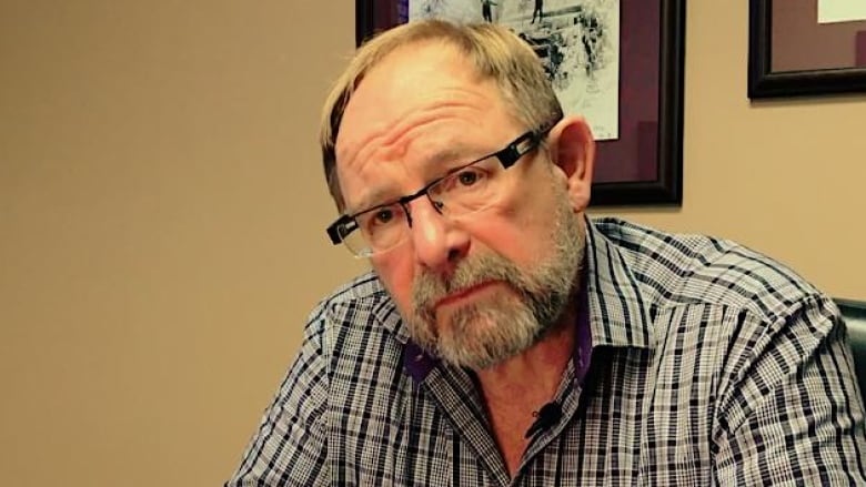 A white man wearing a checked shirt poses for a picture.