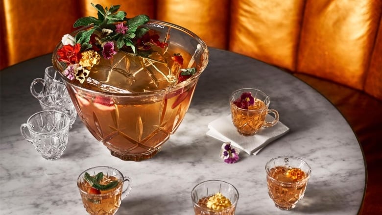 A crystal punch bowl filled with a golden orange punch. Small glasses of punch sit next to it. They're all on a marble table. 