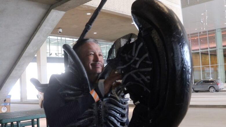 A smiling man wears an alien costume.