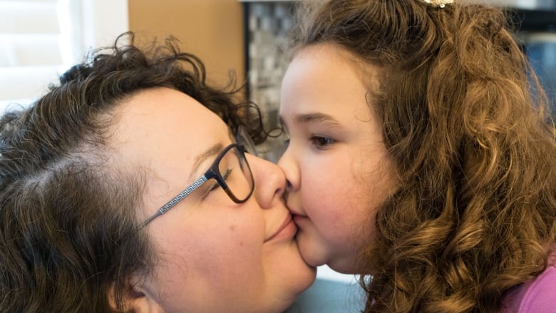 A dark-haired woman receives a kiss from a young child.