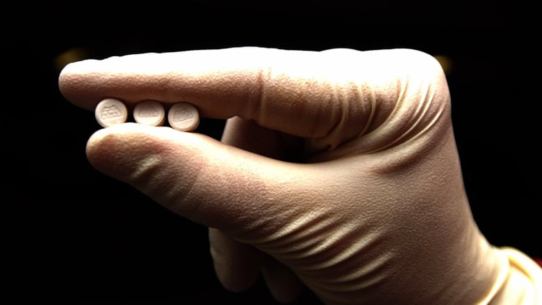 A gloved hand holds three white pills.