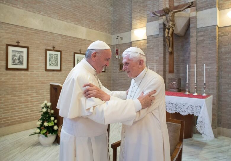 Two men in white robes embrace.