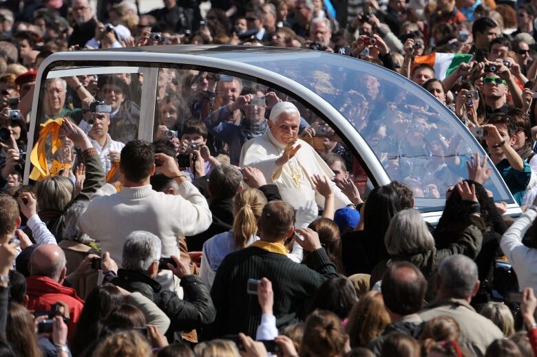 The Pope is shown in a clear vehicle as it drives past a large crowd.