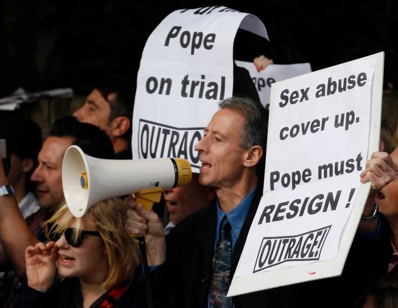 A man with a megaphone holds a sign as part of a protest.