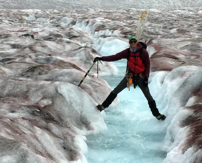 A man stretches his legs across a crevice in a glacier. 