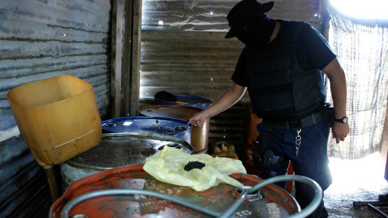 A man wearing a black facemask examines a series of gas canisters with holes on them.