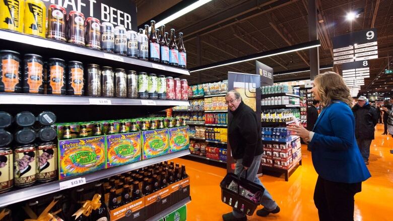 Shoppers pass beer on grocery store shelves. 