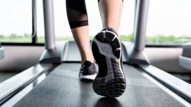 A close up view of a treadmill from behind, showing the lower half of a person's legs and their sneakers.