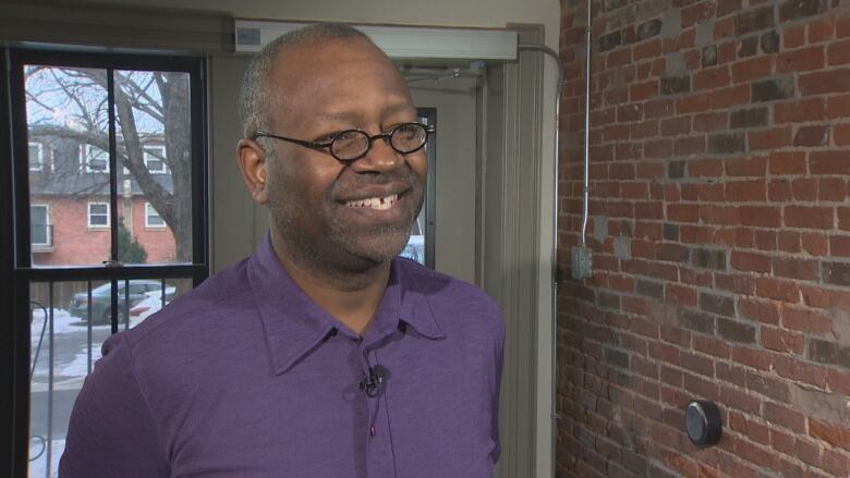 A Black man wearing glasses and a purple button up short sleeved shirt