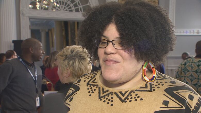 A Black woman with curly hair is wearing a patterned top