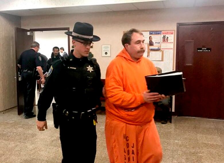 A heavyset man with a mustache is escorted by a law enforcement official at a courthouse in Lockeport, N.Y.