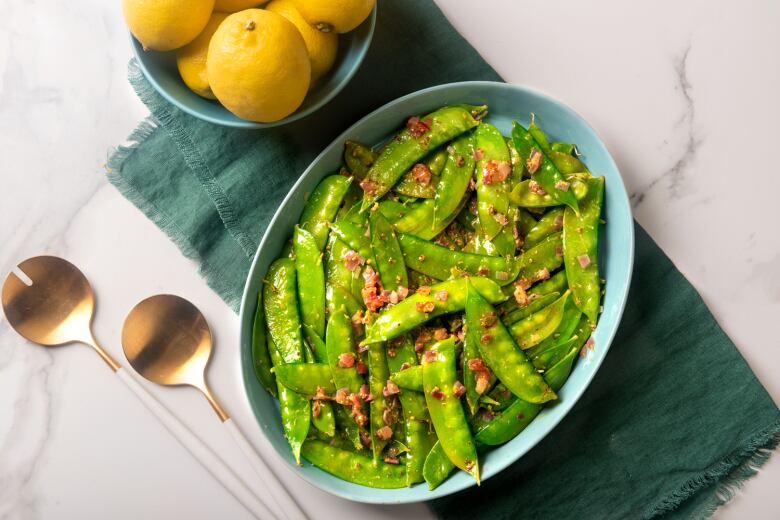 A light blue serving dish of sauted snow peas. 