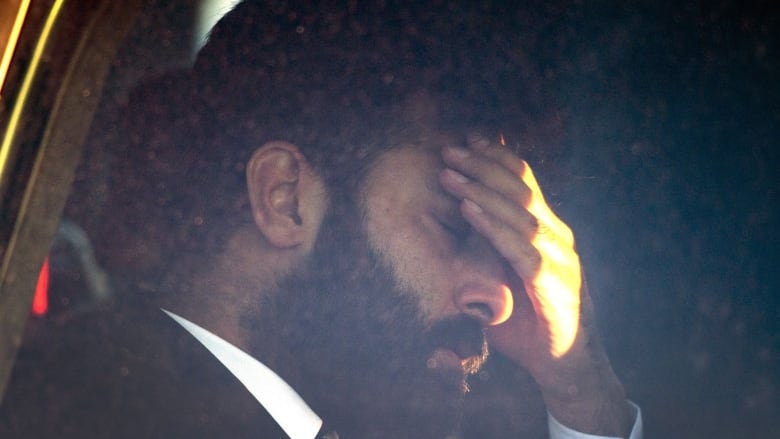 A man with a beard holds his hand on his forehead.