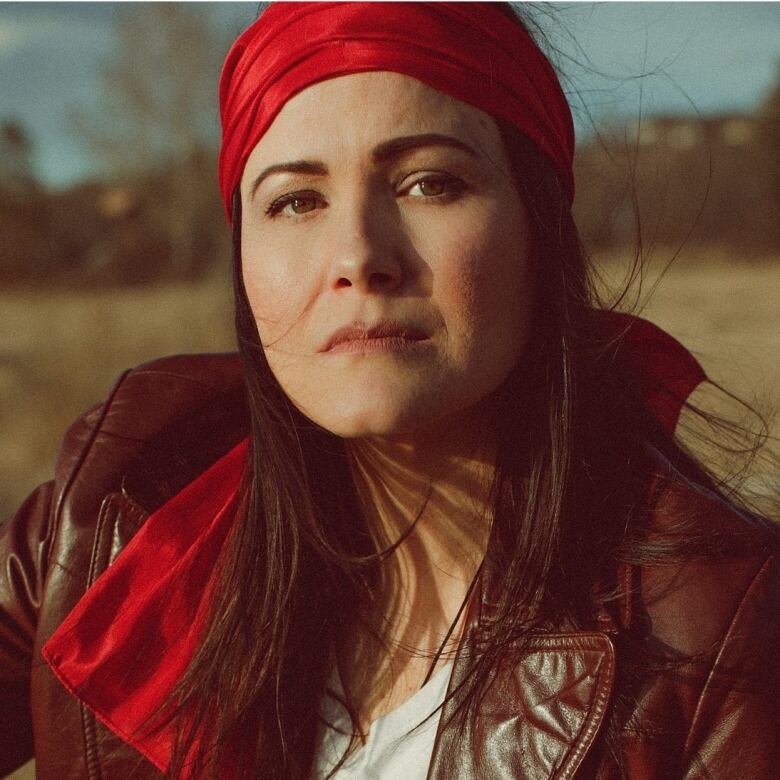 Eekwol in a red headband, standing outside with her hair blowing in the wind