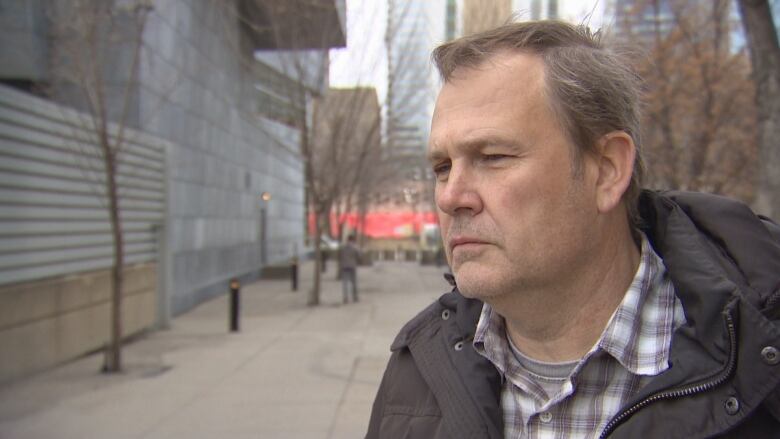 Man dressed in button down shirt and jacket stands near the Edmonton courthouse.