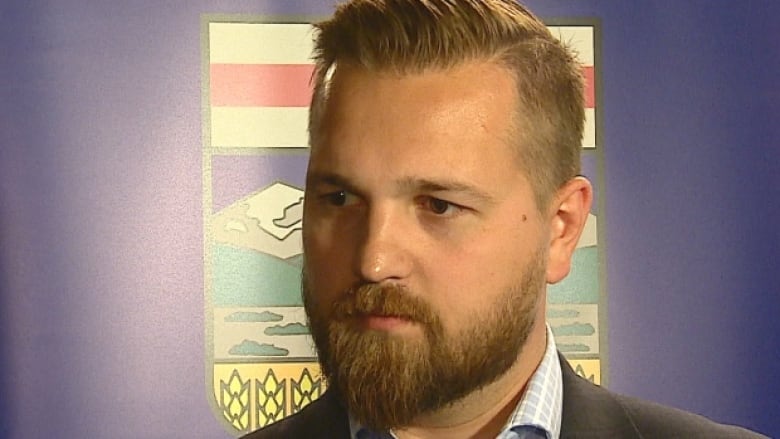 A bearded man in front of an Alberta flag. 