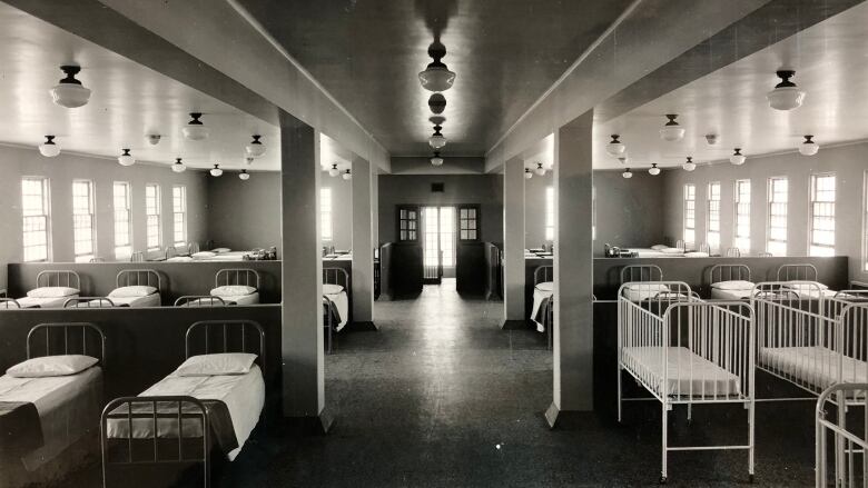 Black-and-white photo of a dormitory with beds on either side.