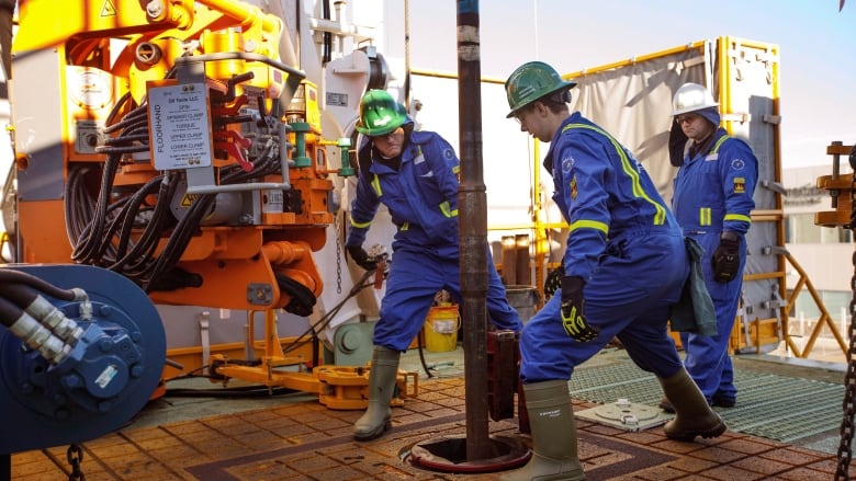 Three men in blue coveralls working on a drilling rig