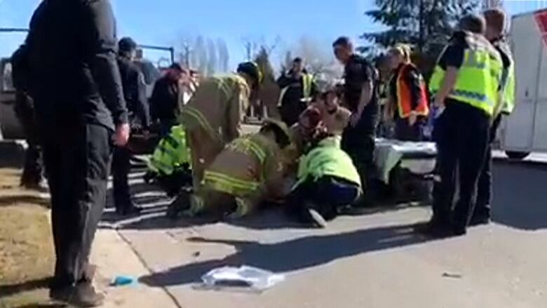 Firefighters and paramedics gather around an injured RCMP officer lying on a roadway.