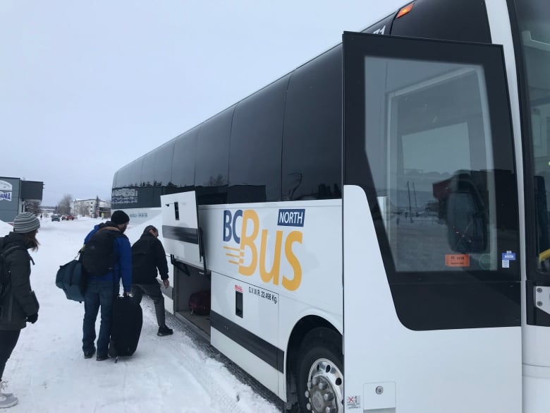 A group of people board a bus with the title 'BC Bus North' on a snowy road.