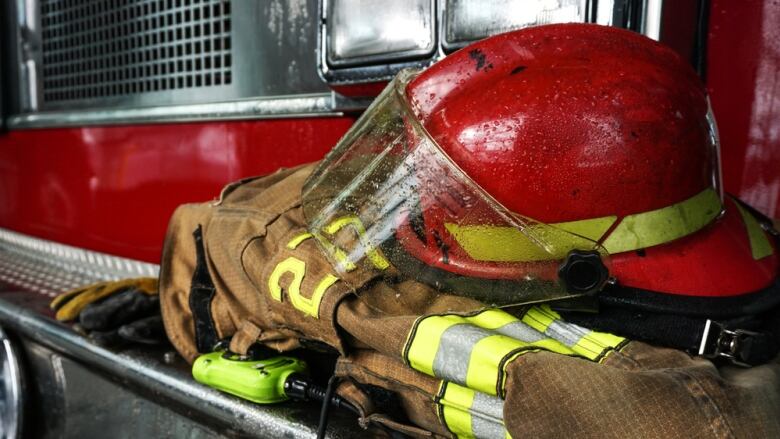 A firefighter uniform is folded up under a fire helmet. They are both resting on the front bumper of a fire truck