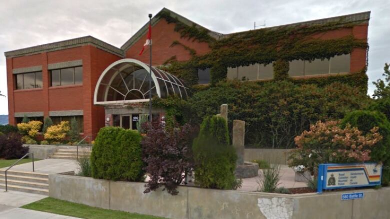 A long, red building with a peaked roof and an entrance arch with an RCMP sign outside.