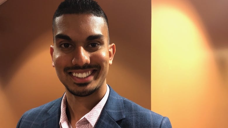 A smiling man in a suit looks at the camera.