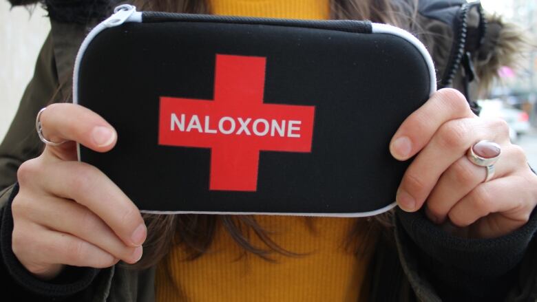 A person holds a black pouch that reads naloxone. 