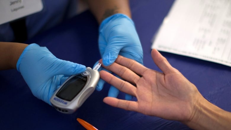 Hands wearing blue gloves giving diabetes test to another person's hands. 