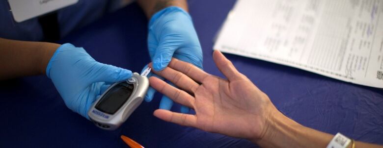 Hands wearing blue gloves giving diabetes test to another person's hands. 