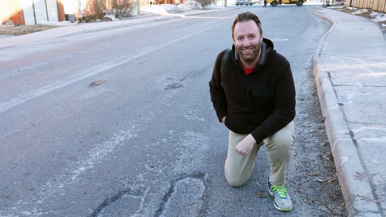 A man kneels beside a pothole