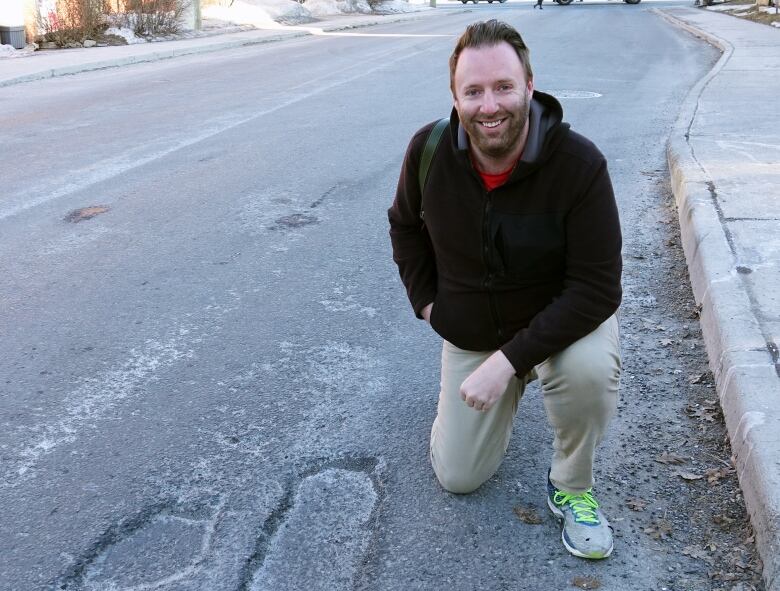 A man kneels beside a pothole