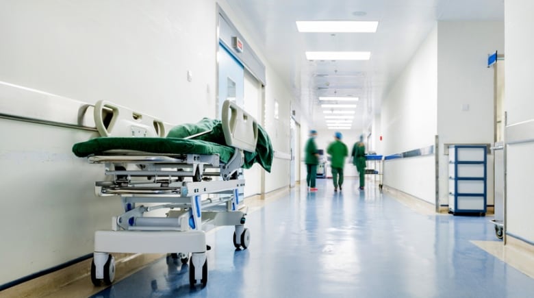 A bed stretcher in a hall. People in scrubs can be seen walking down the hall.