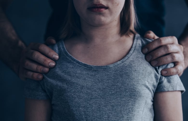 Two adult hands hold the shoulders of an unidentified pre-teen girl. 